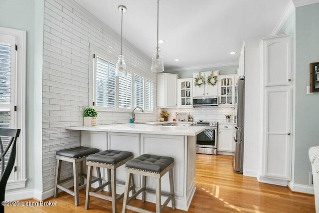 kitchen featuring a peninsula, decorative backsplash, appliances with stainless steel finishes, a kitchen breakfast bar, and light wood-type flooring