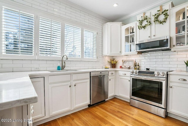 kitchen featuring a sink, tasteful backsplash, stainless steel appliances, light wood-style floors, and crown molding