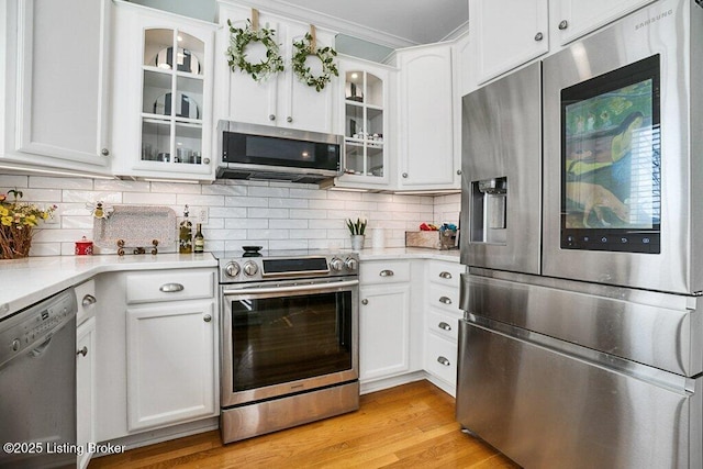 kitchen with backsplash, appliances with stainless steel finishes, white cabinets, and light wood-type flooring