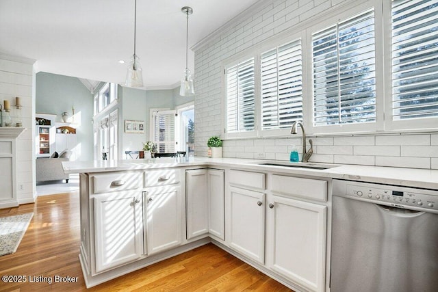 kitchen with a sink, stainless steel dishwasher, a peninsula, crown molding, and light countertops