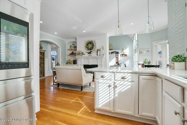 kitchen featuring crown molding, light countertops, arched walkways, and light wood finished floors