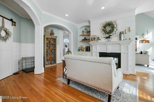 living room with light wood-style flooring, a glass covered fireplace, recessed lighting, arched walkways, and crown molding