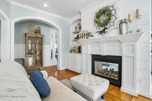 living area featuring light wood-type flooring, recessed lighting, arched walkways, crown molding, and a multi sided fireplace