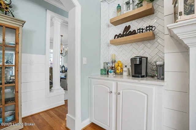 bar with decorative backsplash, light wood-style floors, and decorative columns