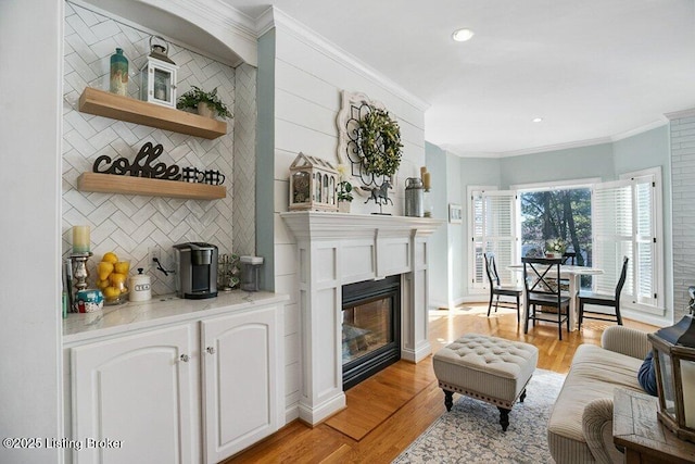 living area featuring a glass covered fireplace, baseboards, light wood-style flooring, and crown molding