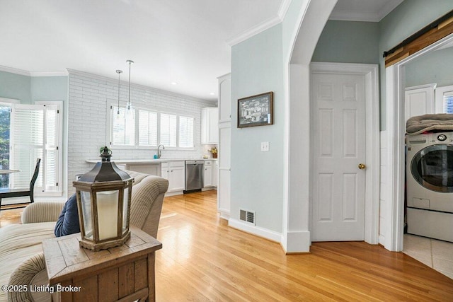 living area featuring light wood finished floors, visible vents, crown molding, washer / dryer, and arched walkways