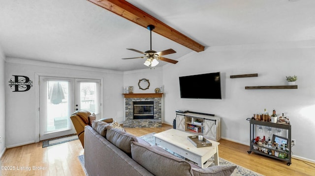 living room featuring vaulted ceiling with beams, baseboards, a stone fireplace, wood finished floors, and a ceiling fan