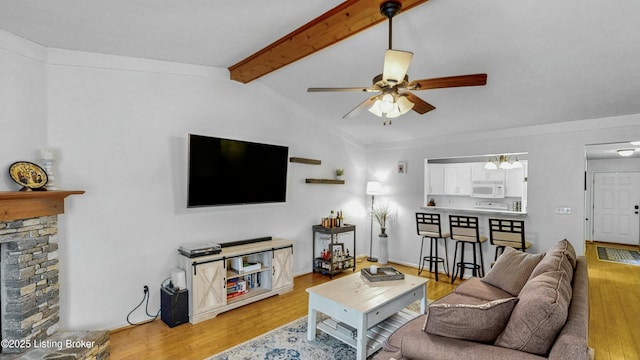 living area featuring a ceiling fan, vaulted ceiling with beams, a fireplace, and light wood-type flooring