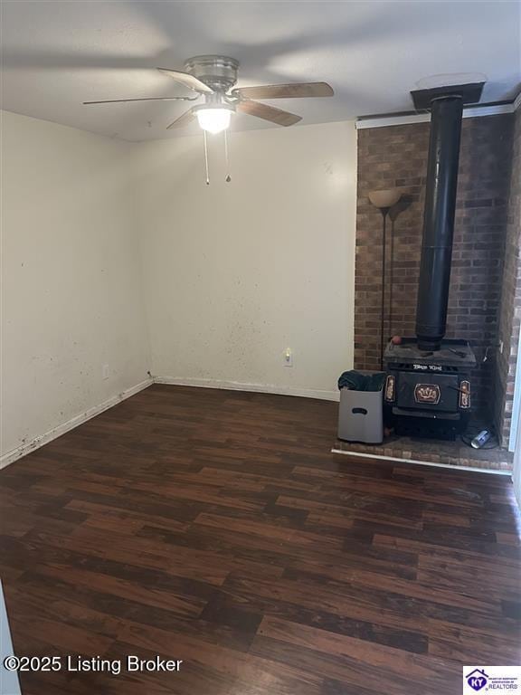 unfurnished living room featuring baseboards, a wood stove, ceiling fan, and wood finished floors