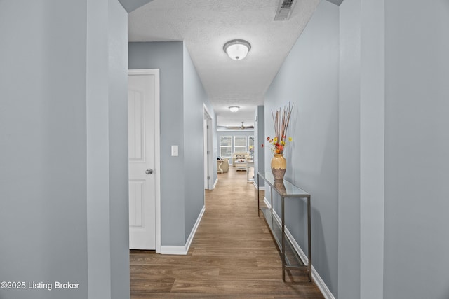 hallway with visible vents, baseboards, a textured ceiling, and wood finished floors