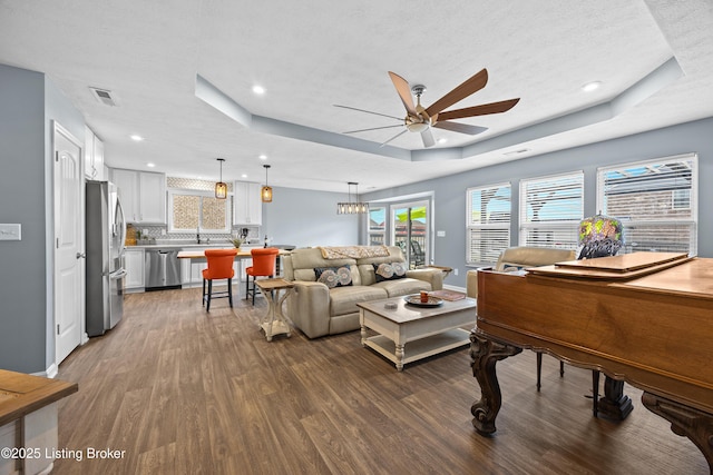 living area with wood finished floors, a ceiling fan, visible vents, a tray ceiling, and a wealth of natural light