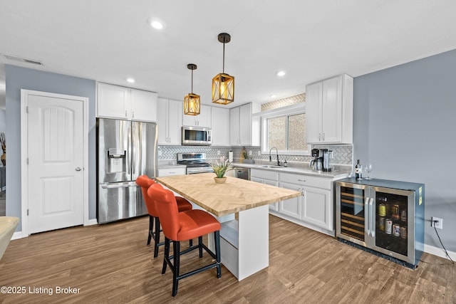 kitchen featuring wood finished floors, a sink, stainless steel appliances, wine cooler, and white cabinets