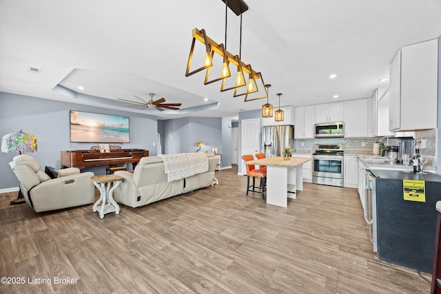 living area featuring ceiling fan, baseboards, light wood-type flooring, and a tray ceiling