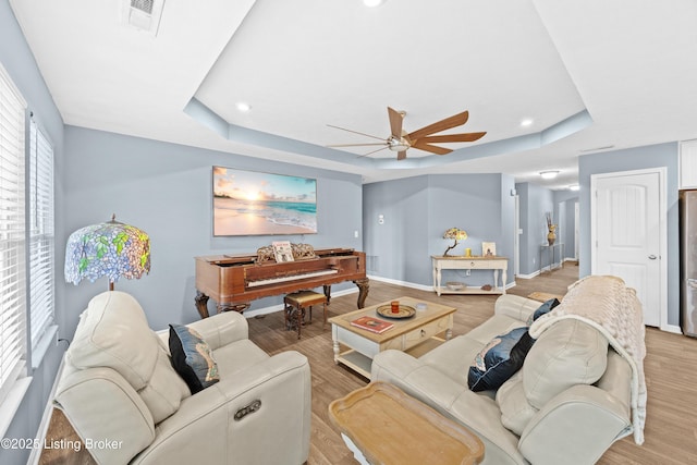 living room featuring visible vents, light wood-style flooring, a raised ceiling, and a ceiling fan