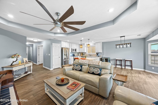 living room featuring a raised ceiling, wood finished floors, a ceiling fan, and baseboards