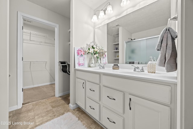 full bathroom featuring a sink, a walk in closet, double vanity, and a shower stall