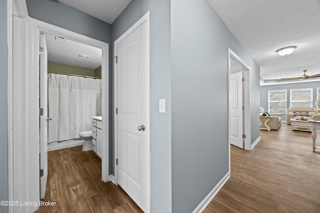 corridor with dark wood-type flooring, baseboards, and a textured ceiling