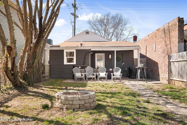 back of house featuring a lawn, a fire pit, and fence