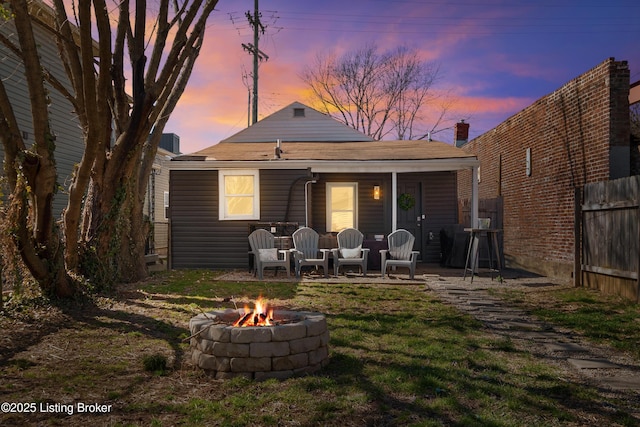 rear view of property with a lawn, an outdoor fire pit, and fence