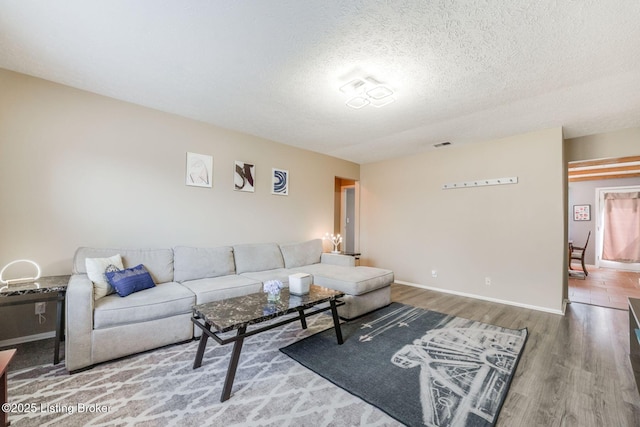 living room featuring visible vents, wood finished floors, baseboards, and a textured ceiling