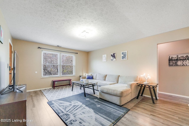 living room featuring light wood-style flooring, a textured ceiling, and baseboards