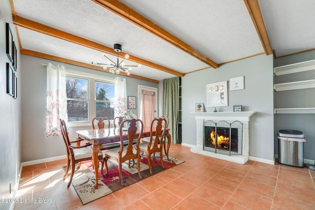 tiled dining space with a brick fireplace, baseboards, beamed ceiling, an inviting chandelier, and a textured ceiling