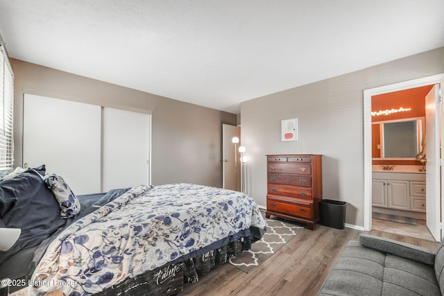 bedroom featuring connected bathroom, light wood-style floors, baseboards, and a sink