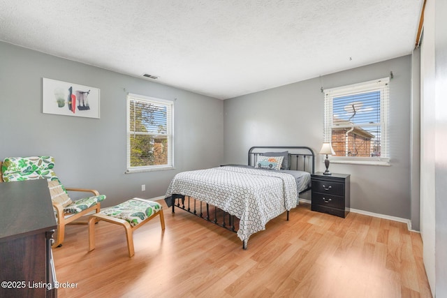 bedroom featuring visible vents, baseboards, light wood-style floors, and a textured ceiling