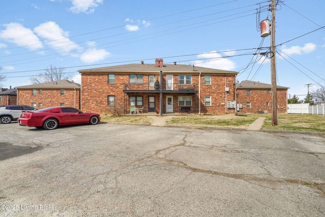 view of front of home with brick siding, a balcony, a front lawn, and fence