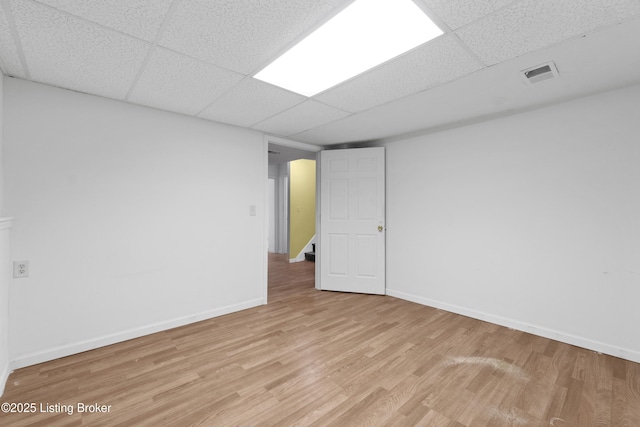 empty room with wood finished floors, visible vents, a drop ceiling, and baseboards