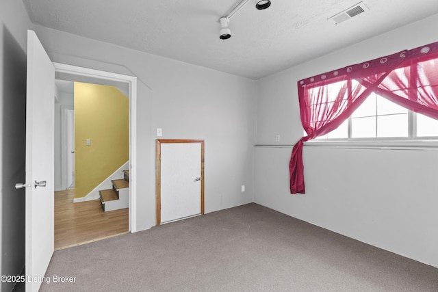 empty room featuring visible vents, carpet flooring, a textured ceiling, and stairs