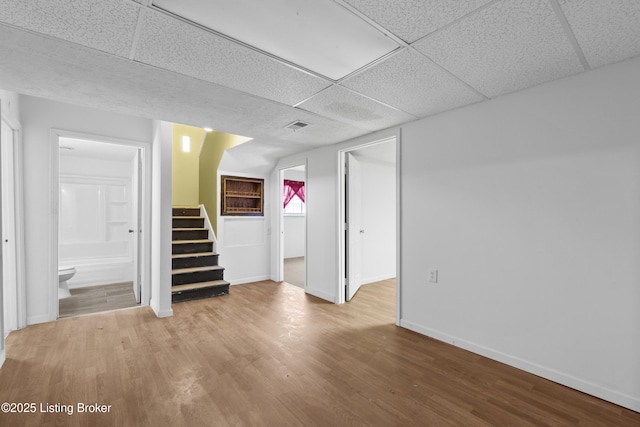 below grade area with stairs, wood finished floors, baseboards, and a paneled ceiling