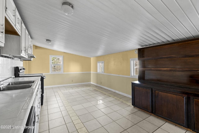 kitchen featuring range with electric cooktop, white cabinets, light tile patterned floors, baseboards, and vaulted ceiling