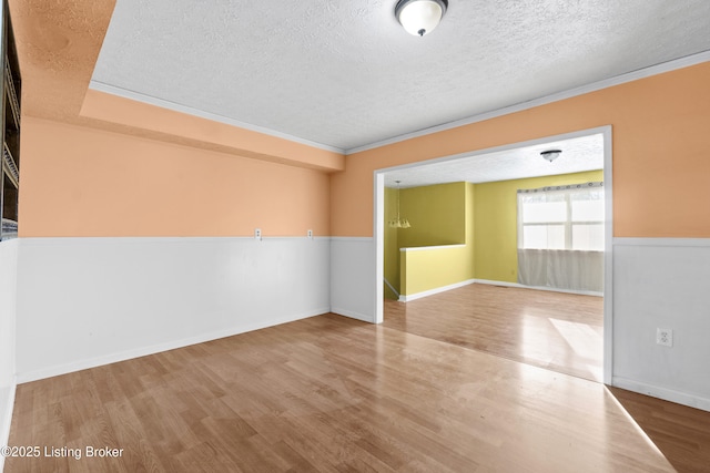 empty room featuring baseboards, a textured ceiling, wood finished floors, and ornamental molding