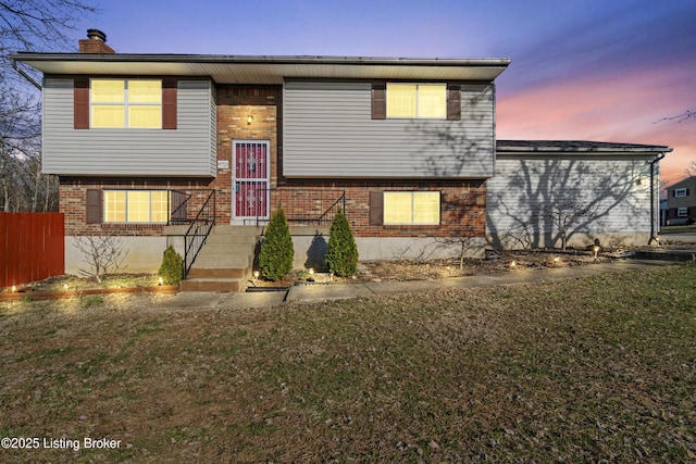 raised ranch with brick siding, a lawn, a chimney, and fence