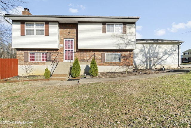 raised ranch featuring a front yard, brick siding, and a chimney