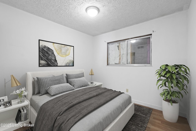 bedroom featuring a textured ceiling, baseboards, and wood finished floors