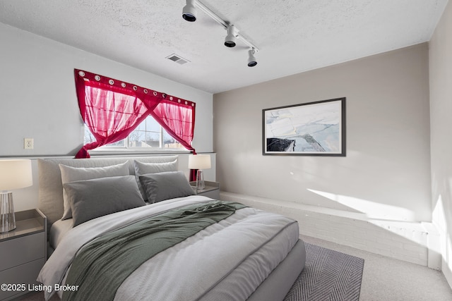 bedroom featuring rail lighting, visible vents, a textured ceiling, and carpet flooring