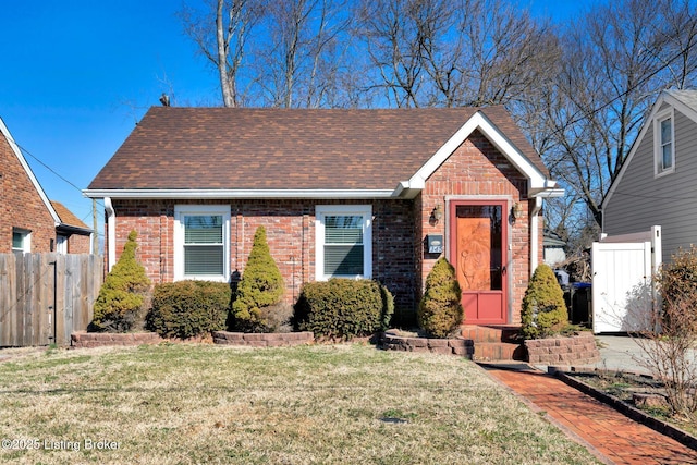 bungalow with a front lawn, fence, brick siding, and roof with shingles