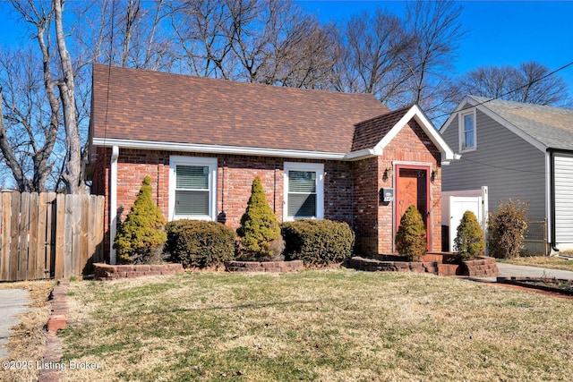 view of front of property featuring brick siding, roof with shingles, a front lawn, and fence