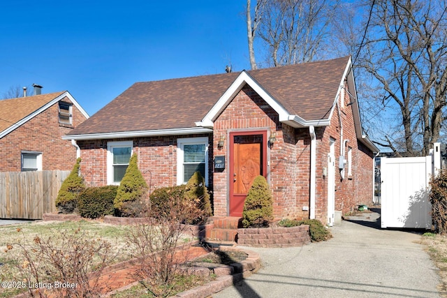 view of front of property featuring brick siding, a shingled roof, and fence