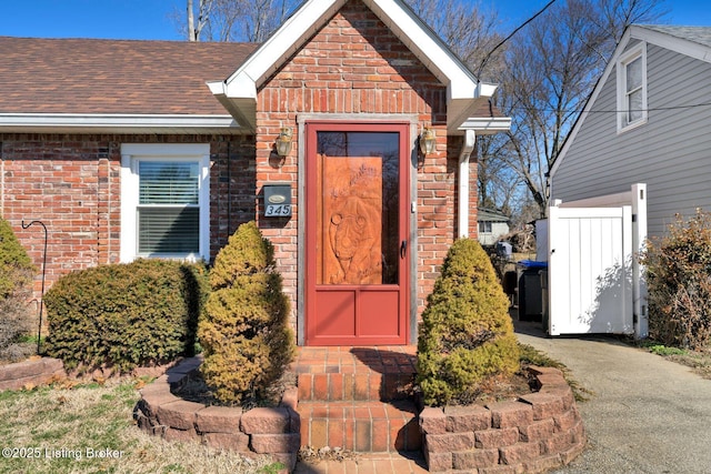 doorway to property featuring brick siding and a shingled roof