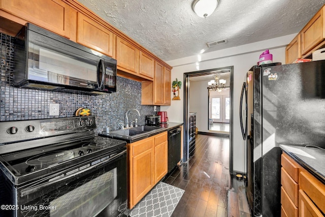 kitchen featuring visible vents, black appliances, a sink, dark countertops, and dark wood-style floors