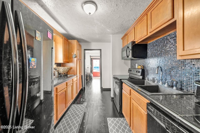 kitchen featuring dark wood-style floors, a sink, decorative backsplash, black appliances, and dark countertops