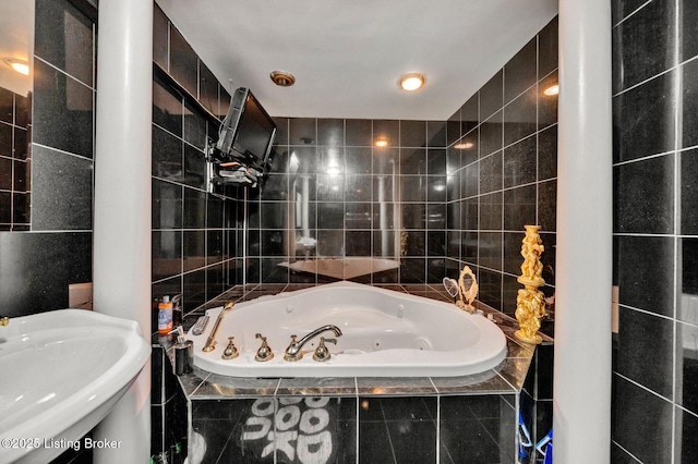 bathroom with a tub with jets, tile walls, and a sink