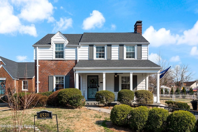 view of front of home featuring brick siding, fence, roof with shingles, covered porch, and a chimney