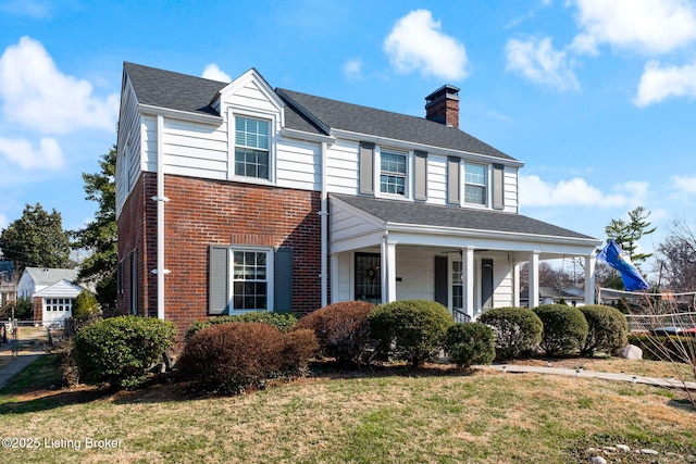 view of front facade featuring brick siding, fence, a front yard, roof with shingles, and a chimney