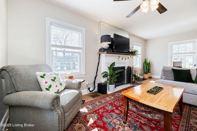 living room featuring wood finished floors, baseboards, a fireplace with flush hearth, and ceiling fan