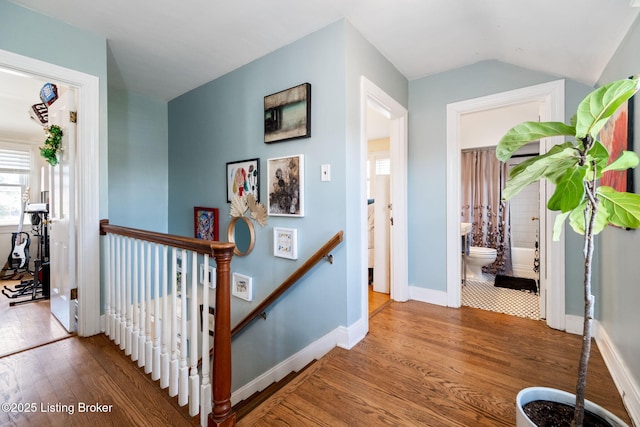 stairway featuring baseboards, wood-type flooring, and vaulted ceiling