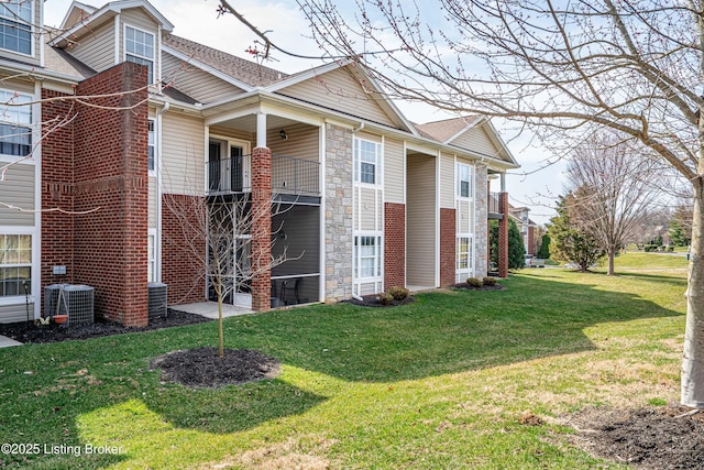 view of home's exterior featuring a balcony, central AC unit, a lawn, and stone siding